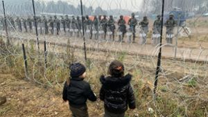 Kein Durchkommen. Kinder stehen in einem Flüchtlingslager nahe der belarussisch-polnischen Grenze. Auf der anderen Seite des Zaunes verhindern polnische  Soldaten, dass die Migranten die Grenze überschreiten. Foto: dpa/Henadz Zhinkov