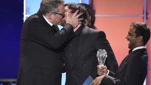 Adam McKay, links, schmatzt Christian Bale bei dessen Triumph in der Kategorie „Beste Komödie“  für “The Big Short”.  Aziz Ansari, der die Auszeichnung überreicht, freut’s. Foto: dpa