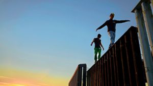 Zwei Migranten aus Mittelamerika balancieren bei Tijuana auf dem Grenzzaun zwischen Mexiko und den USA. Foto: dpa/Gregory Bull