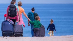 Urlauber und Tagesgäste gehen mit ihrem Reisegepäck an den Strand an der Ostseeküste in Warnemünde. Foto: dpa/Jens Büttner
