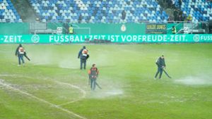 Arbeiter versuchten, Wasserlachen vom Spielfeld zu entfernen. Foto: dpa/Uwe Anspach
