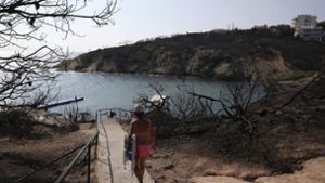 Eine Frau geht beim griechischen Badeort Rafina hinunter zum Strand. Rechts und links vom Weg sieht man, wie das Feuer vor zehn Tagen gewütet hat. Foto: AP